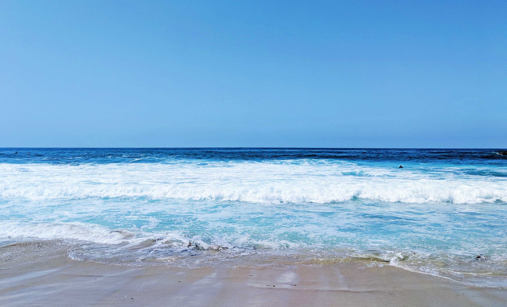 A photo of blues skies, ocean waves and wet beach sand